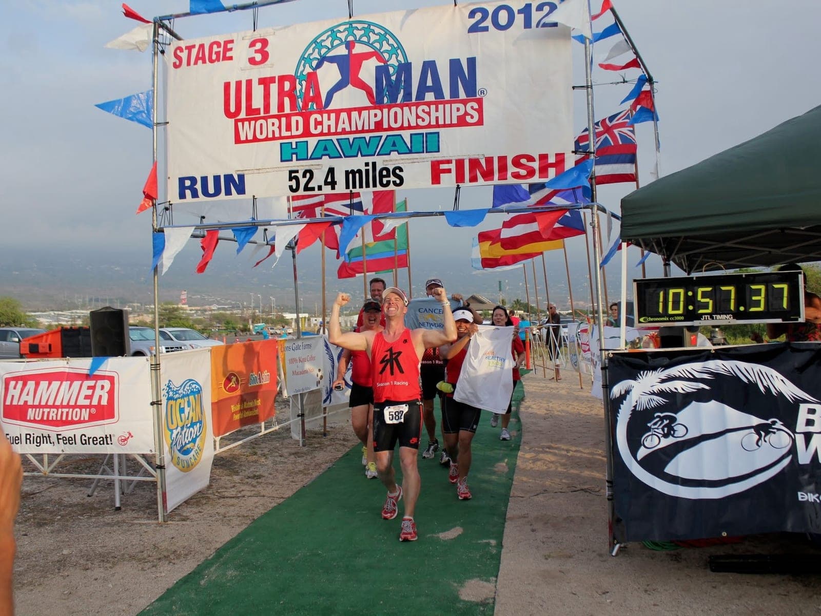 The author finishing the Ultraman World Championships in Hawaii, arms raised at the line as other finishers come in behind him.